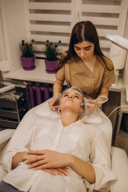 Kozmetik uzmanı, güzellik salonundaki güzel, genç bir kadının yüz derisinin mikro cilt bakımını yapıyor. Kozmetoloji ve profesyonel cilt bakımı..