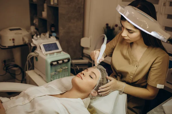 Beautician applying hydro gel mask on the young woman face, before laser treatment in beauty salon. Close up side view.