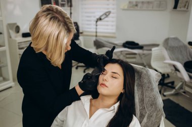 Permanent tattoo makeup on eyelashes of eyes of young woman in beauty salon.
