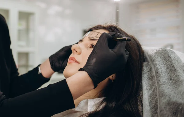 Changing the shape of the brows. Stylist measuring the eyebrows with the ruler. Micropigmentation work flow in a beauty salon. Woman having her eye brows tinted with Semi-permanent makeup.