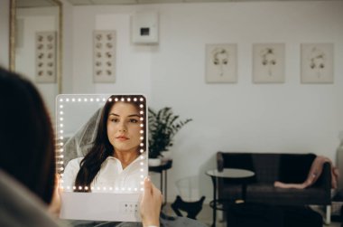 Usta ve müşteri, kalıcı kaşlarını ve dudaklarını düzelttikten sonra aynaya bakıyor. Makyaj yapıyor ve birlikte gülümsüyor.