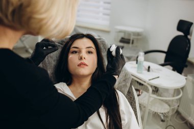 Beautician hand doing eyebrow permanent makeup on a pretty woman face