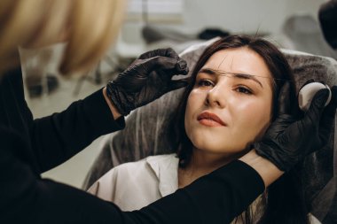 The make-up artist plucks eyebrows with a thread close-up. Women's cosmetology in the beauty salon.