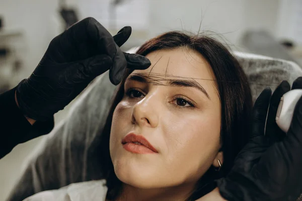 The make-up artist plucks eyebrows with a thread close-up. Women\'s cosmetology in the beauty salon.