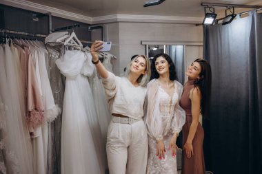 Güzel gelin zarif bir gelinlik modern düğün salonda üzerinde çalışıyor, onun arkadaşlar yardımcı