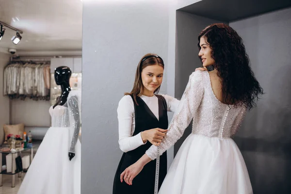 Female making adjustment to wedding gown in fashion designer studio. Bride wearing her wedding gown with female dress designer making final adjustments on dress.