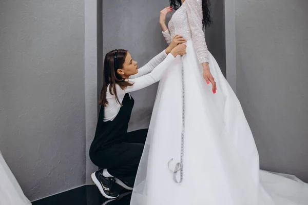 Female making adjustment to wedding gown in fashion designer studio. Bride wearing her wedding gown with female dress designer making final adjustments on dress.