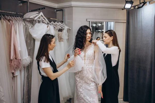Bride at the clothes shop for wedding dresses. she is choosing a dress and the designer are assisting her
