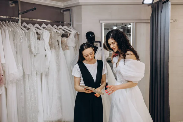 Bride at the clothes shop for wedding dresses. she is choosing a dress and the designer are assisting her