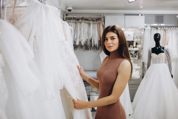 Woman choosing wedding dress in a showroom. Future bride buying a wedding gown in a shop.