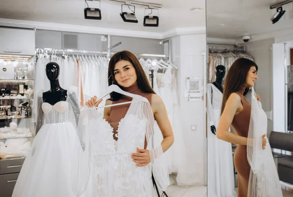 Woman choosing wedding dress in a showroom. Future bride buying a wedding gown in a shop.
