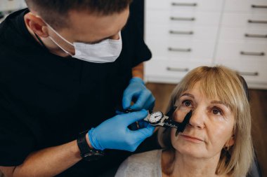 Estetik cerrahi konsültasyonunda yaşla ilgili kırışıklıkların ortadan kaldırılmasıyla ilgili yaşlı bir kadın. Gubo-chin kıvrılır, ağzın kenarları aşağı iner. Yüzün alt üçte birinin düzeltilmesi.