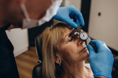 A plastic surgeon examines old eye wrinkles in an elderly woman. Clinic of modern plastic surgery