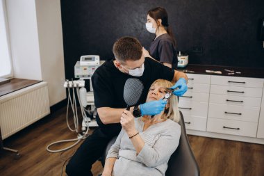 Happy elderly woman enjoying her beautiful toothy smile looking to the mirror in the dental office