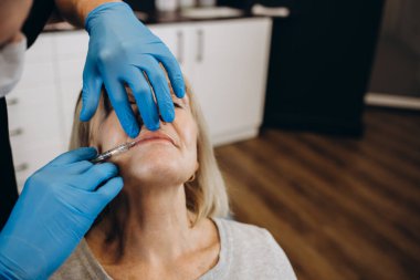 Güzellik, estetik cerrahi ve kozmetik kavramı - kadın kıdemli ve cerrah el ile mavi arka plan üzerinde şırınga