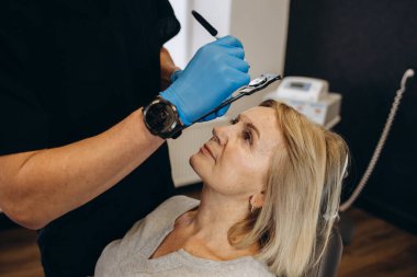 marking the face of an elderly woman old of plastic surgery at a reception at the doctor