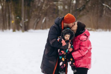 Happy family with daughter having fun in winter forest. Mom, dad, daughter running and walking in the snow in mountains. Father, mother, and child in sled walk and play in the park. Winter holidays.