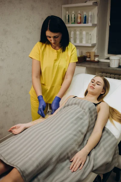 Waxing. Depilation hand and arm of the young woman lying in the spa salon