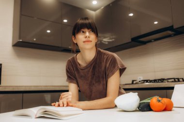 Mutfakta yemek kitabı okuyan genç bir kadın yemek tarifi arıyor..