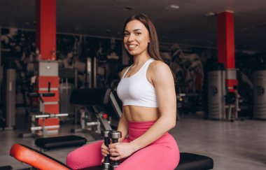 Spor salonundaki bir bankta duran halterci kız.