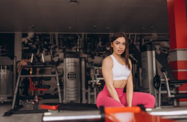 Güzel bir kadın bankta oturur. Koç verimli bir dönemeçten sonra dinleniyor. Spor salonunda kadın sporcu giyimi..