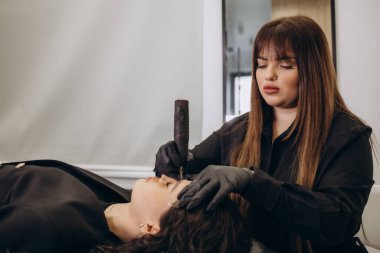 Beautician hand doing eyebrow permanent makeup on a pretty woman face