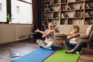 Mutlu orta yaşlı 50 'ler çifti evde meditasyon yapmayı öğreniyor. İnternet sitesinden canlı televizyon yoga dersi izliyorlar. Bilgisayara bakıyor ve sanal eğitim egzersizleri yapıyorlar..