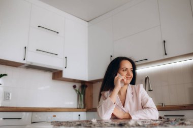 Akıllı telefonlu mutlu bir kadın laptopta çalışırken cep telefonundan inanılmaz güzel haberler alıyor. Kazanan el hareketi yapıyor, işi başarıyla kutluyor, başarıyı kutluyor.