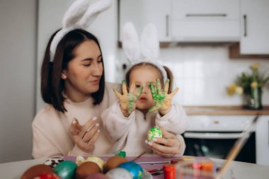 Anne ve kızı yumurta boyuyor. Mutlu aile Paskalya için hazırlanıyor. Tavşan kulağı takan şirin bir kız çocuğu..