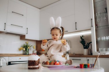 Küçük kız paskalya yumurtalarını boyuyor. Mutlu aile Paskalya için hazırlanıyor. Paskalya günü tavşan kulaklı şirin bir kız..