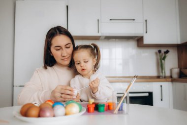 İyi tatiller. Bir anne ve kızı yumurta boyuyor. Aile Paskalya için hazırlanıyor. Sevimli küçük kız tavşan kulağı takıyor..