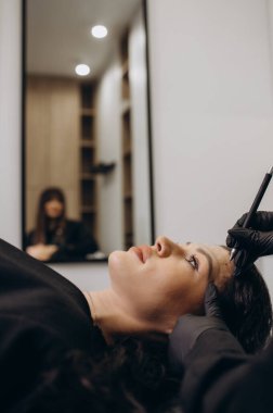 Beautician hand doing eyebrow permanent makeup on a pretty woman face