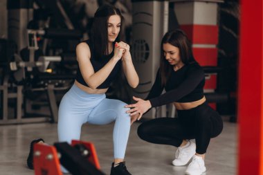 Kadın kişisel antrenör, spor salonunda antrenman yaparken esmer müşterisine tavsiyelerde bulunur..