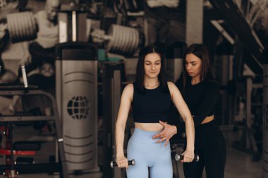 Kadın kişisel antrenör, spor salonunda antrenman yaparken esmer müşterisine tavsiyelerde bulunur..