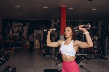 Kolları için egzersiz yapan atletik bir kadın. Spor modeli dambıllarla çalışıyor. Dambıllarla egzersiz yapan bir kadın. Fitness, egzersiz, sağlıklı yaşam ve diyet konsepti.