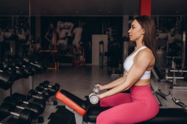 Spor yaptıktan sonra oturup dinlenen ya da spor salonunda egzersiz yapan sağlıklı genç bir kadın. Kadın spor salonunda mola veriyor ve spor giyim kuşamında suyla rahatlıyor. Fitness konsepti, Sağlıklı, Spor, Yaşam Tarzı