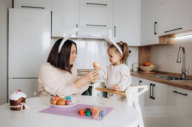 Paskalya, anne ve kızı Paskalya yumurtalarını boyarlar, gülümser ve tatillerini evde, mutfakta, bir tavşanın kulaklarında geçirirler..