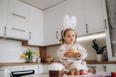 Çocuk paskalya yumurtası boyuyor. Çocuklarla yaratıcılık. Masanın arkasında yumurta, fırça, yumurta, bayram bayrakları olan bir kızın elleri. Kendin yap. Paskalya için el işleri ve el işleri. ÇEVİR