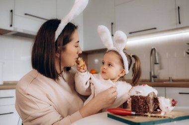 Paskalya yumurtaları, dekoratif tavşanlar ve lalelerin yanında Paskalya ekmeğine bakan heyecanlı anne ve çocuk.
