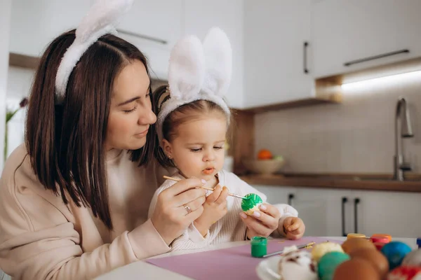 stock image Mother and her daughter with painting eggs. Happy family celebrate Easter. Cute little child girl wearing bunny ears.