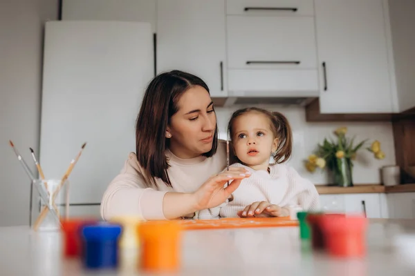 stock image Smiling little girl is drawing a Mother's Day card with a red heart drawn and hugging her mom