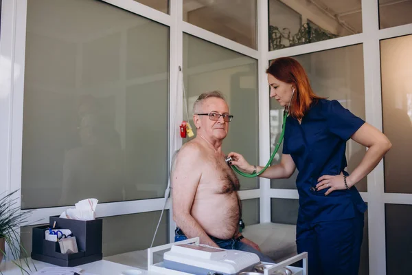 stock image Caring Caucasian female doctor use phonendoscope examine mature male patient heart rate at consultation in hospital. Woman nurse or GP use stethoscope listen to senior man heartbeat in clinic