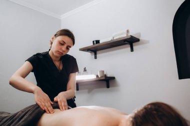 Aydınlık modern klinikte geleneksel masaj yaparken müşterinin sırtına dirseklerle bastıran isimsiz bir kadın masör..