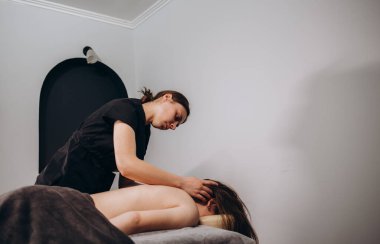 Portrait of a professional female masseuse doing therapeutic massage to her client at the clinic. Concept of relax and body care