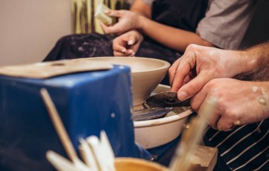 partial view of young african american couple in aprons sculpting pot on wheel with wet sponge in pottery.