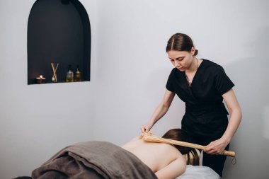 Bambu çubuklarıyla stres önleyici masaj yaptıran bir kadın. Spa Salonu vücut terapisini gençleştiriyor.