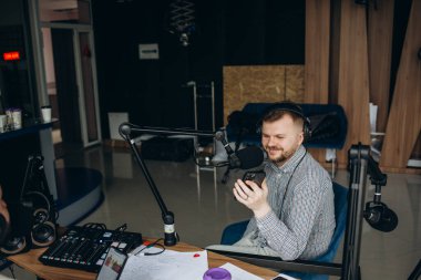 Genç bir radyo sunucusunun portresi içki içiyor, mikrofonla konuşurken odaklanmış görünüyor, canlı bir şovu yönetiyor.