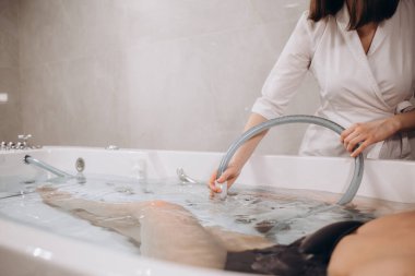 Güzellik salonunda hidromasaj yaparken genç bir kadın. Vücut bakımı ve kaplıca kavramı. Masöz, banyodaki kıza su püskürterek masaj yapar.