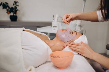 Kozmetik jöle maskesi, yüz bakımı. Kozmetik uzmanı yüzüne spatula sürerek aljinat maskesi takıyor..