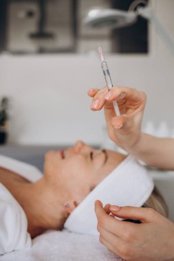 Botulinum toksin şırıngalı bir güzellik uzmanı. Kazın ayaklarını kesmek için iğne yapıyor. Yanak hacmi mezoterapiyi arttırır. Kozmetoloji kliniğinde yaşlanma önleyici tedavi ve yüz gerdirme.